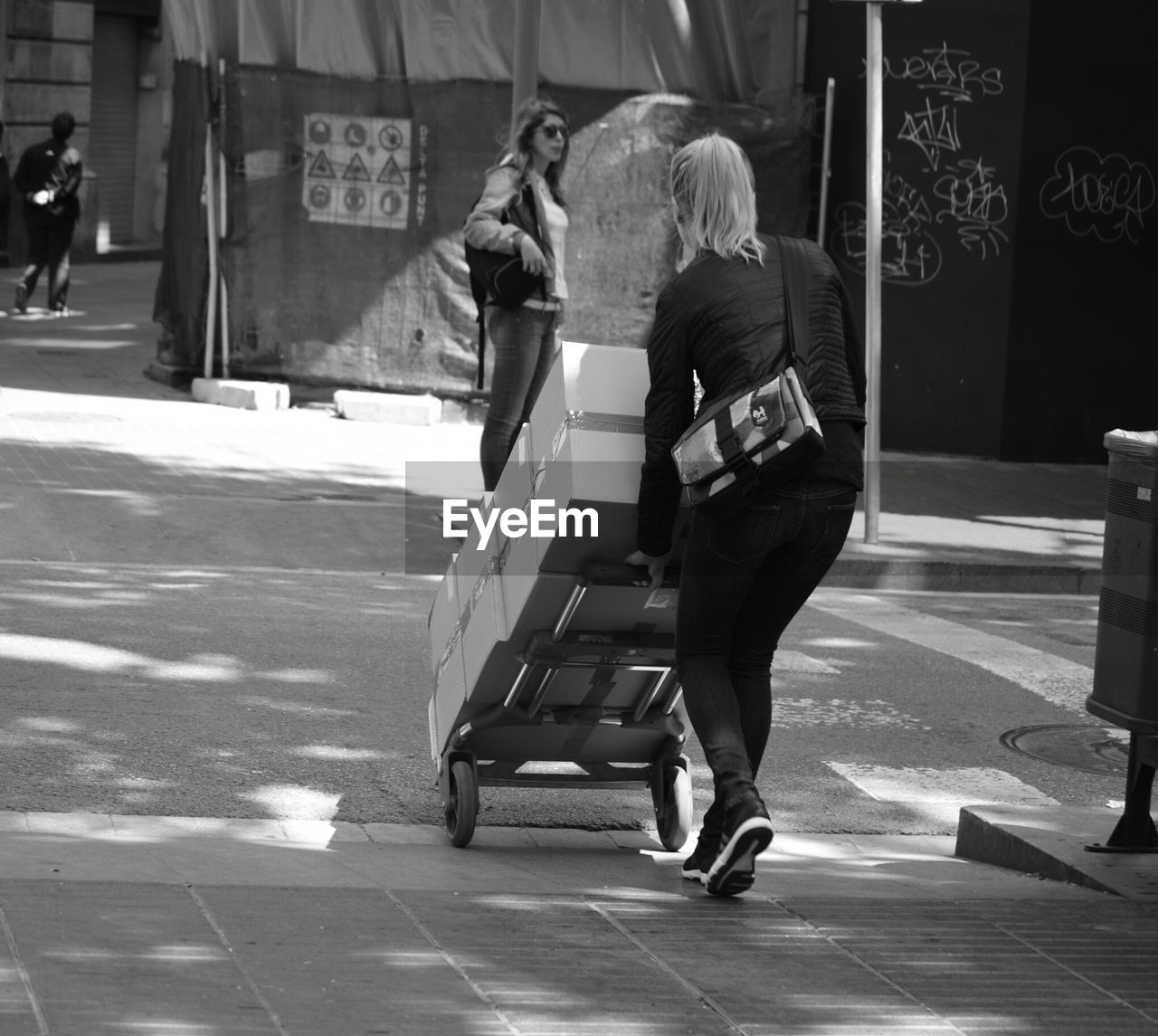 Rear view of woman with boxes on luggage cart at road