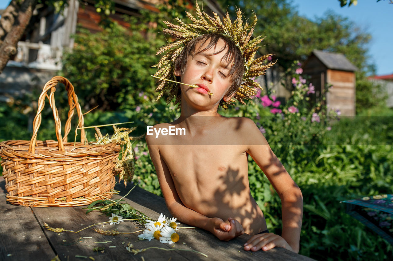 Shirtless boy eating cereal by basket against plants