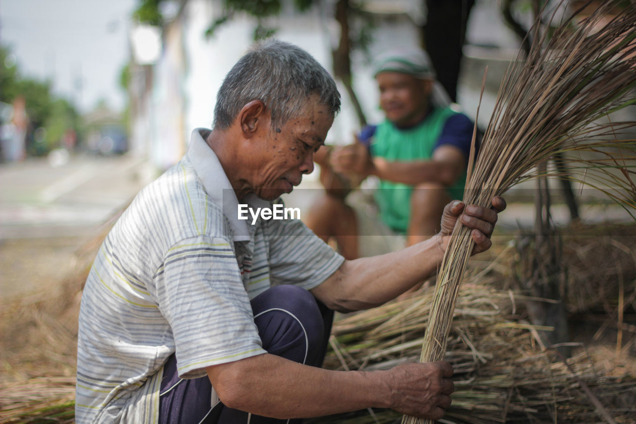Senior man making broom with palm leaves