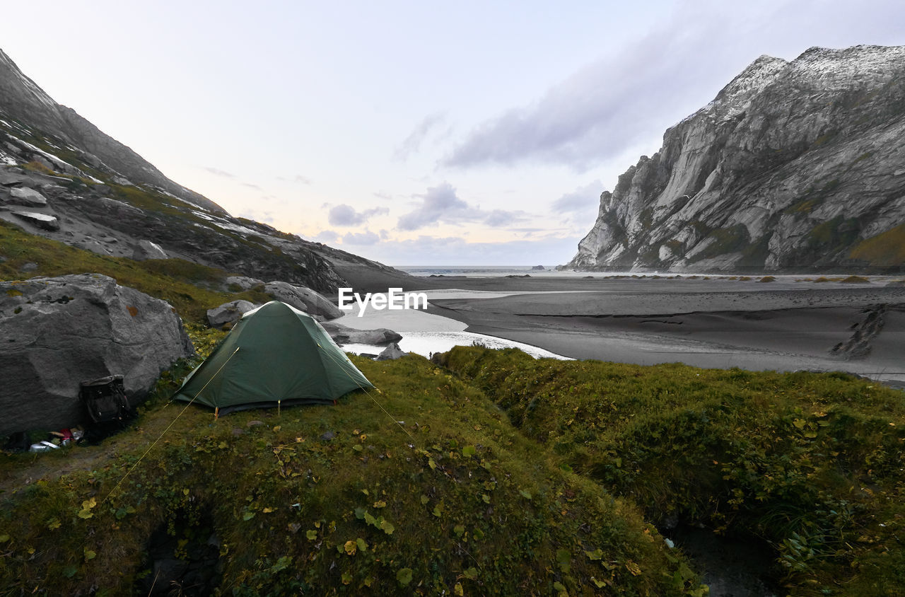 Green tent on hill at bunes beach during sunset with mountains and the ocean  lofoten norway