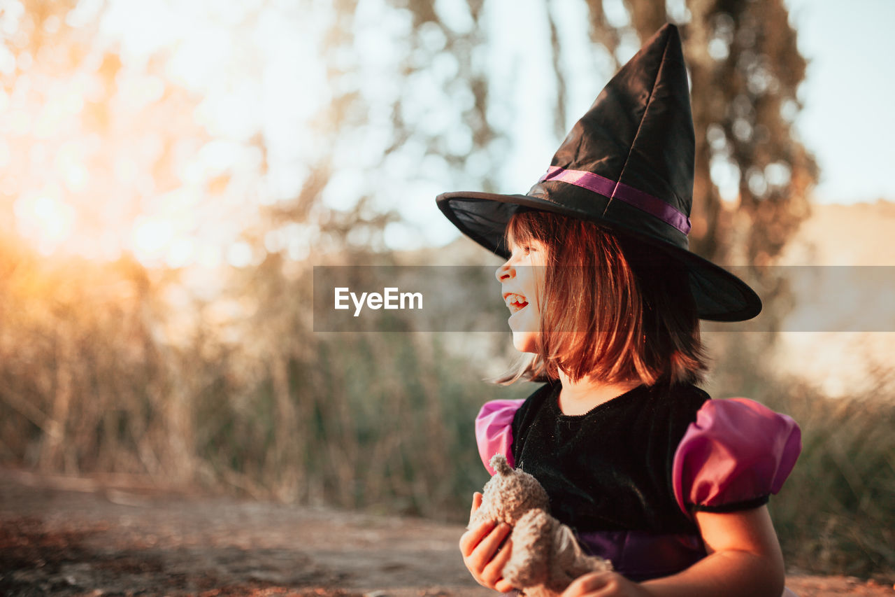 Smiling girl wearing witchs hat during halloween at forest