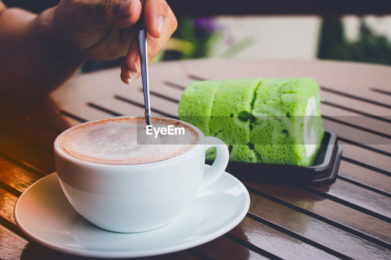 Cropped hand of person stirring coffee in cup on table at cafe