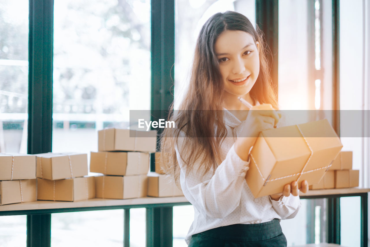 Portrait of young businesswoman writing on package at office