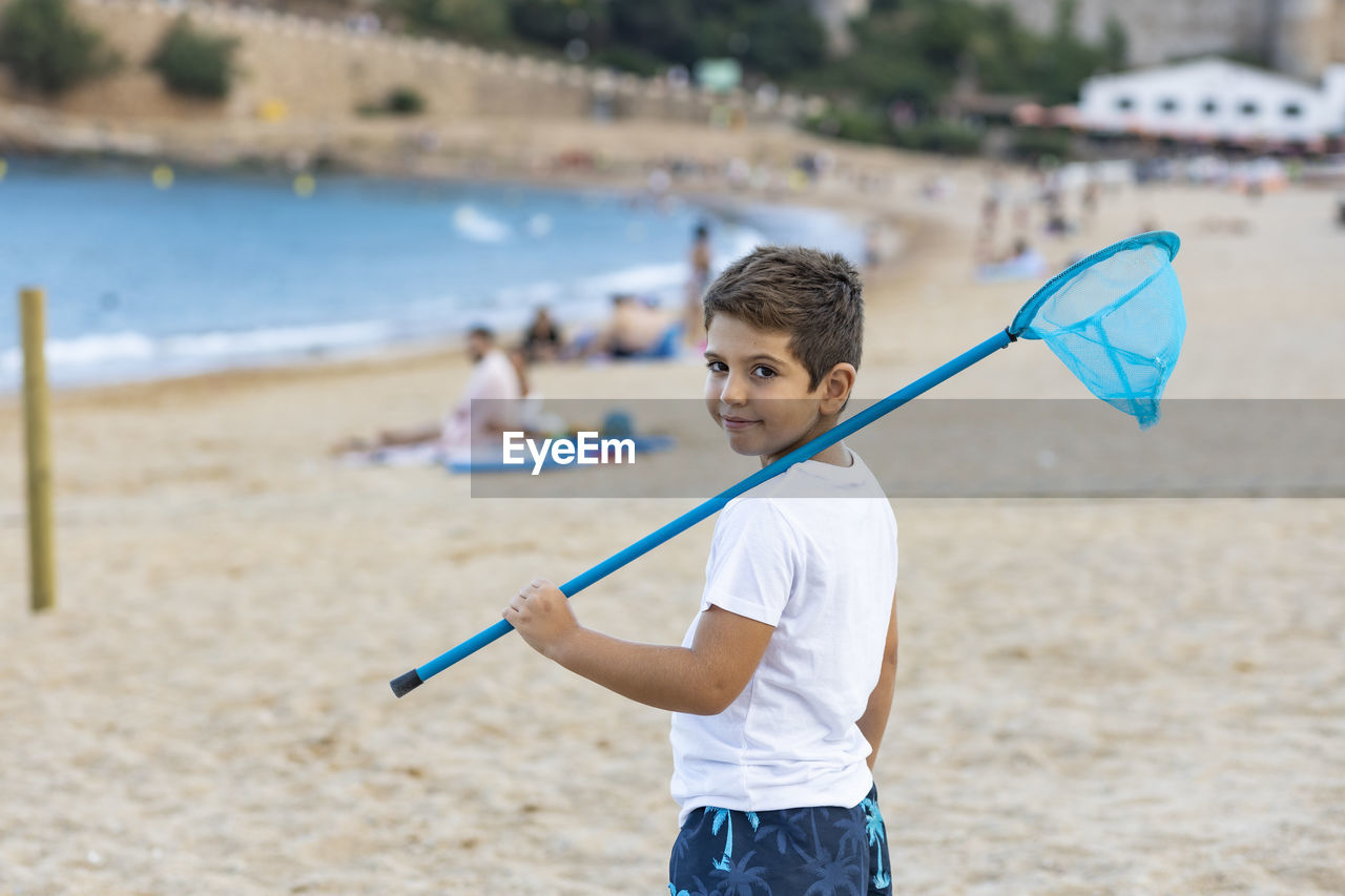 Portrait of boy holding net standing on beach