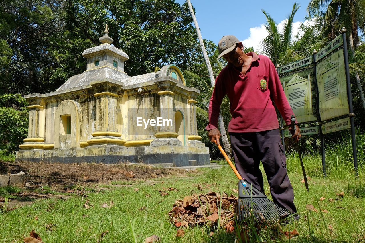 Man cleaning fallen leaves against historic building at park