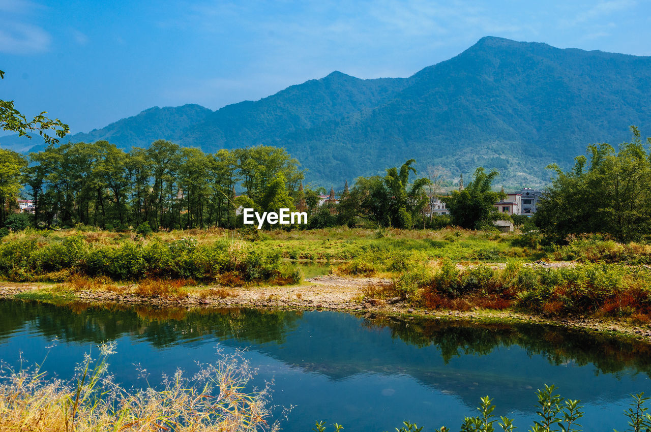 REFLECTION OF TREES IN LAKE AGAINST MOUNTAINS