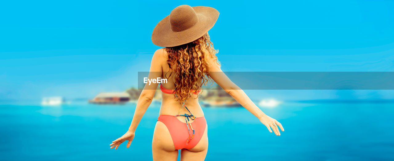 Rear view of woman wearing bikini standing at sea