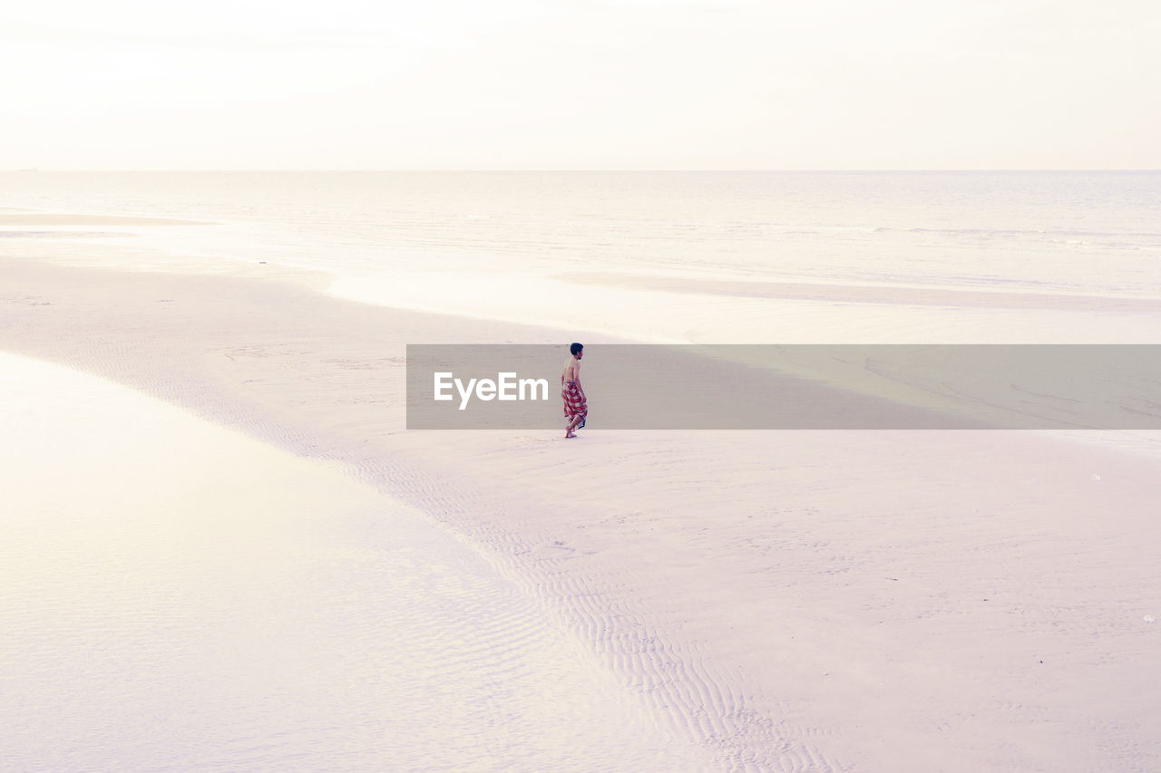 Full length of man walking on sandbar at beach against sky