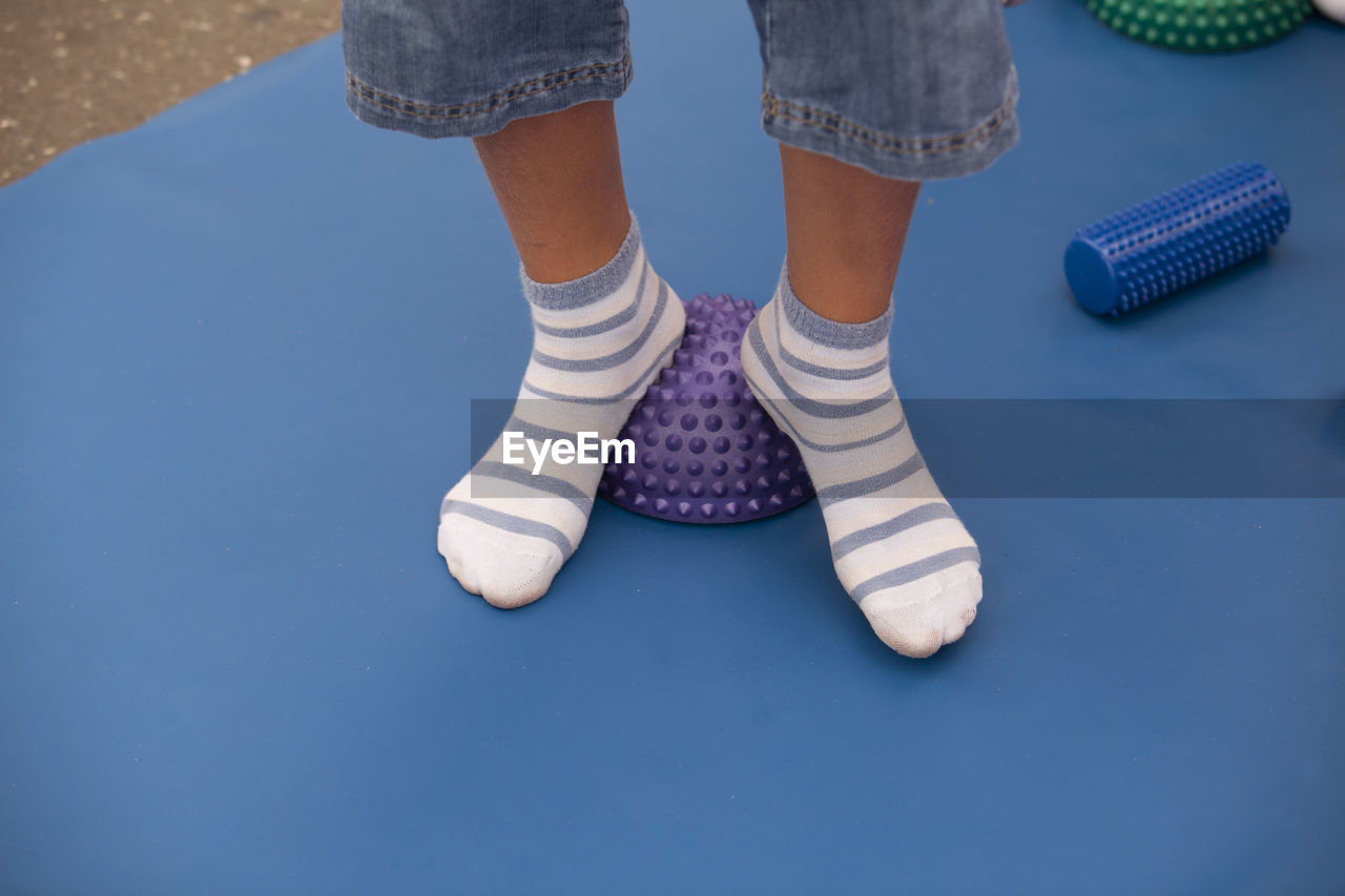 Low section of boy wearing socks standing on spiked balls while exercising in gym