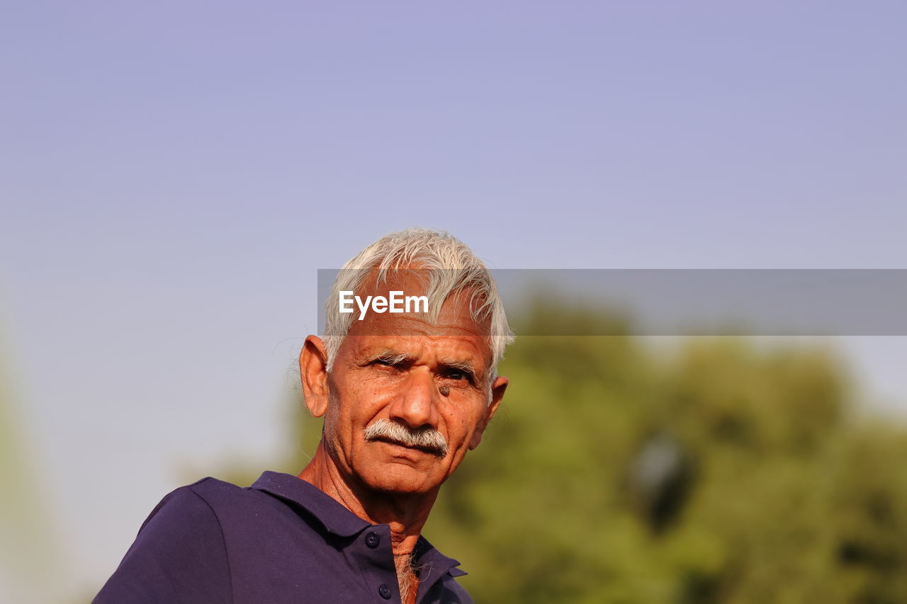 adult, one person, portrait, senior adult, copy space, men, seniors, headshot, smiling, happiness, gray hair, sky, person, emotion, nature, lifestyles, retirement, facial hair, casual clothing, landscape, day, looking, cheerful, rural scene, outdoors, beard, mature adult, looking at camera, relaxation, leisure activity, focus on foreground, enjoyment, human face, front view, clear sky, white hair, sunlight, plant