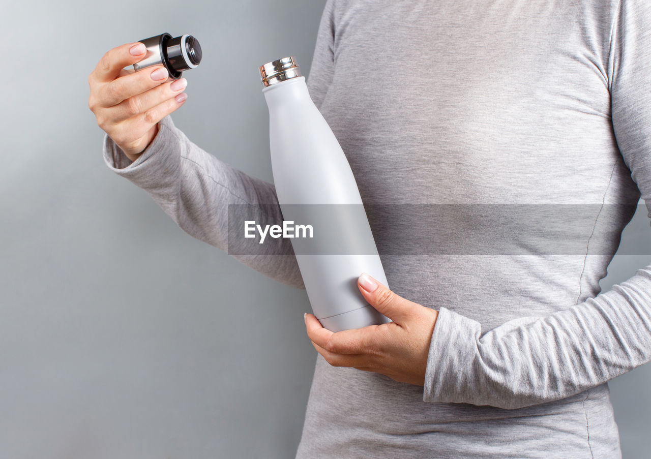 Close up of woman in grey tee holding grey insulated bottle on grey background