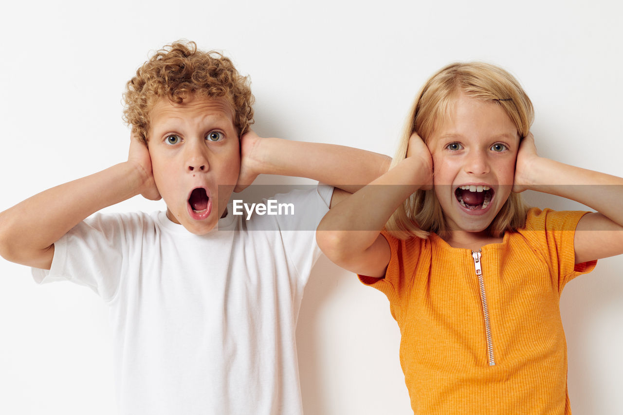 Sibling covering ears against white background