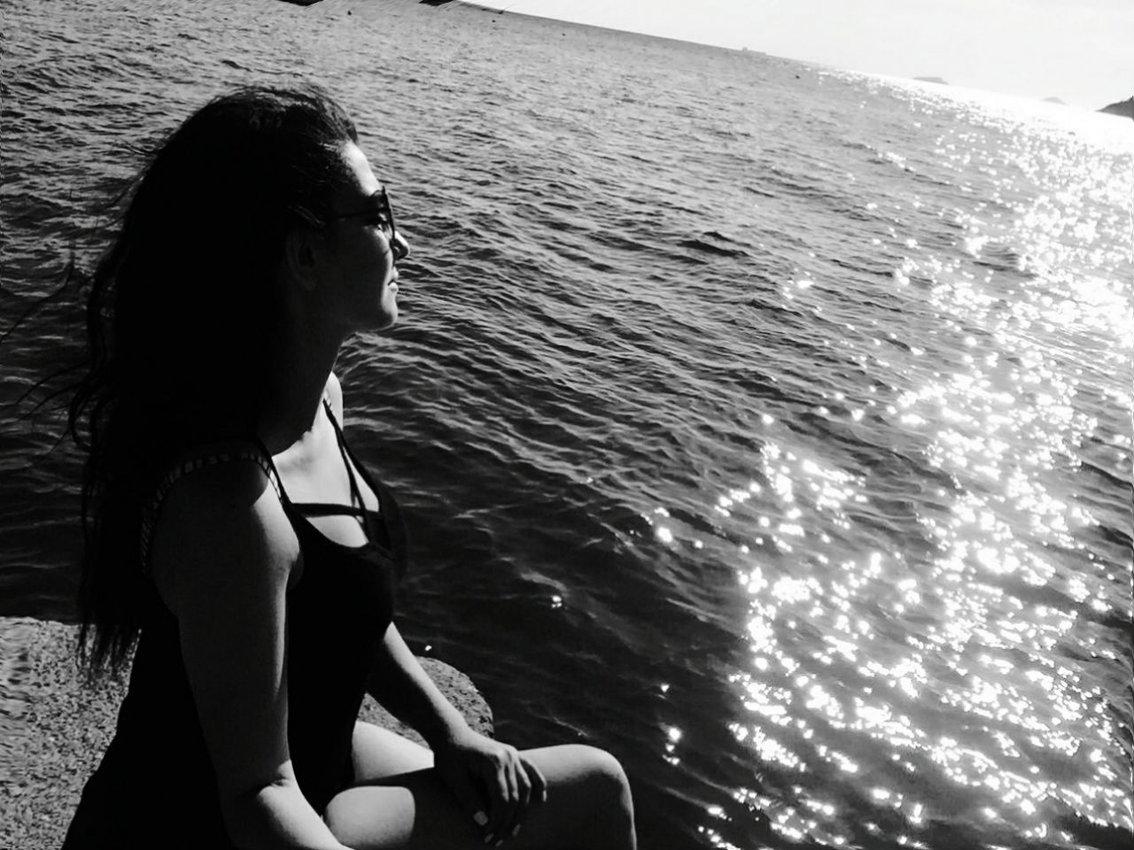 Woman sitting on jetty by sea during sunny day