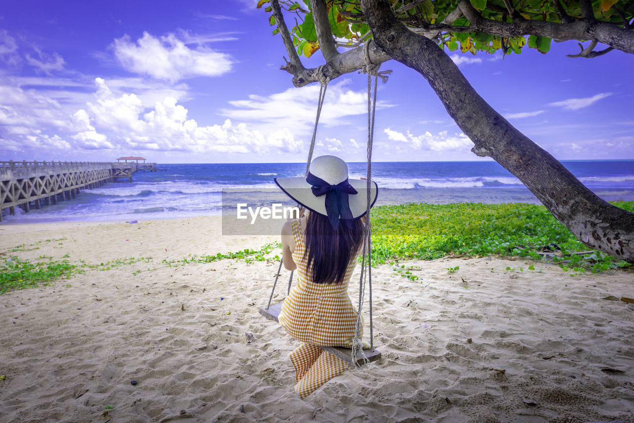 Rear view of woman sitting on swing on beach