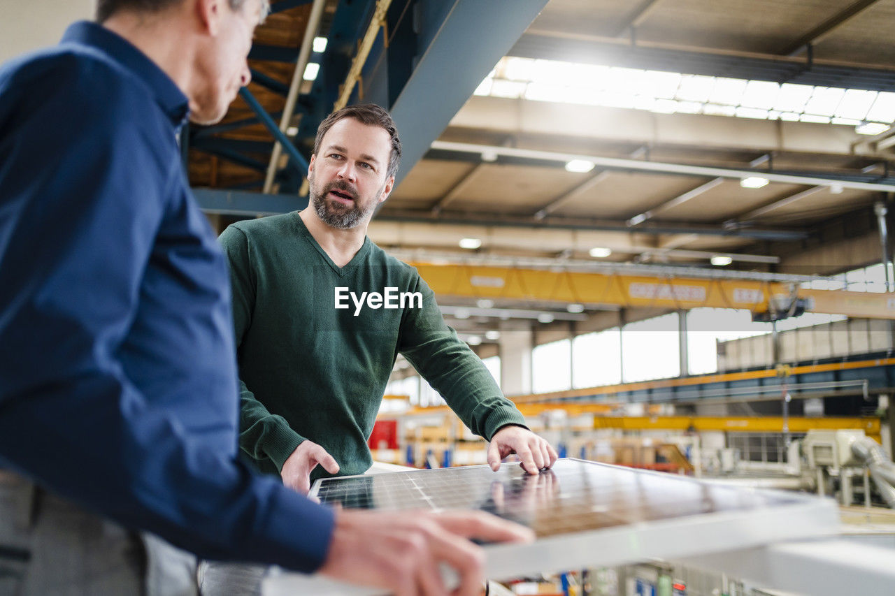 Manager explaining solar panel to businessman at factory