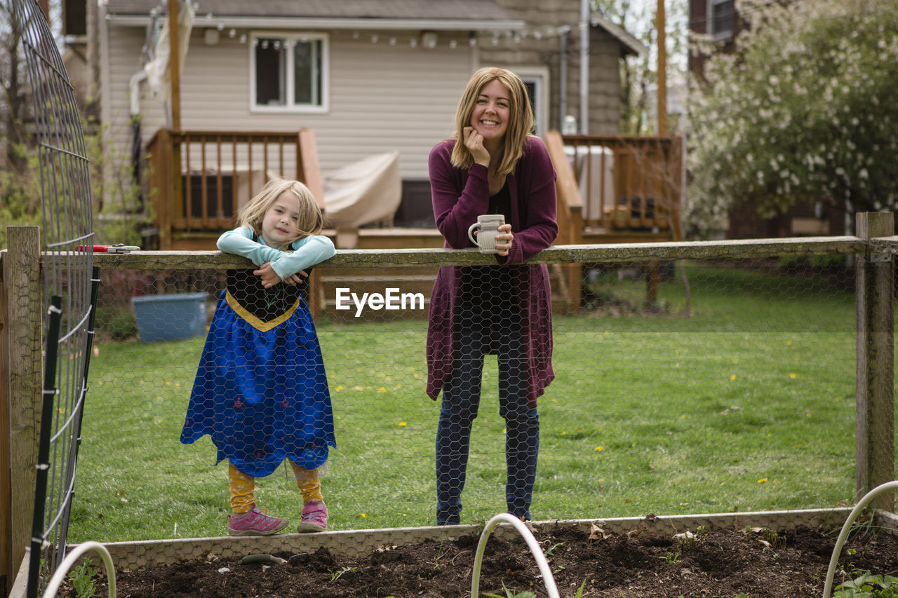 A mother and little girl in princess dress stand at edge of garden