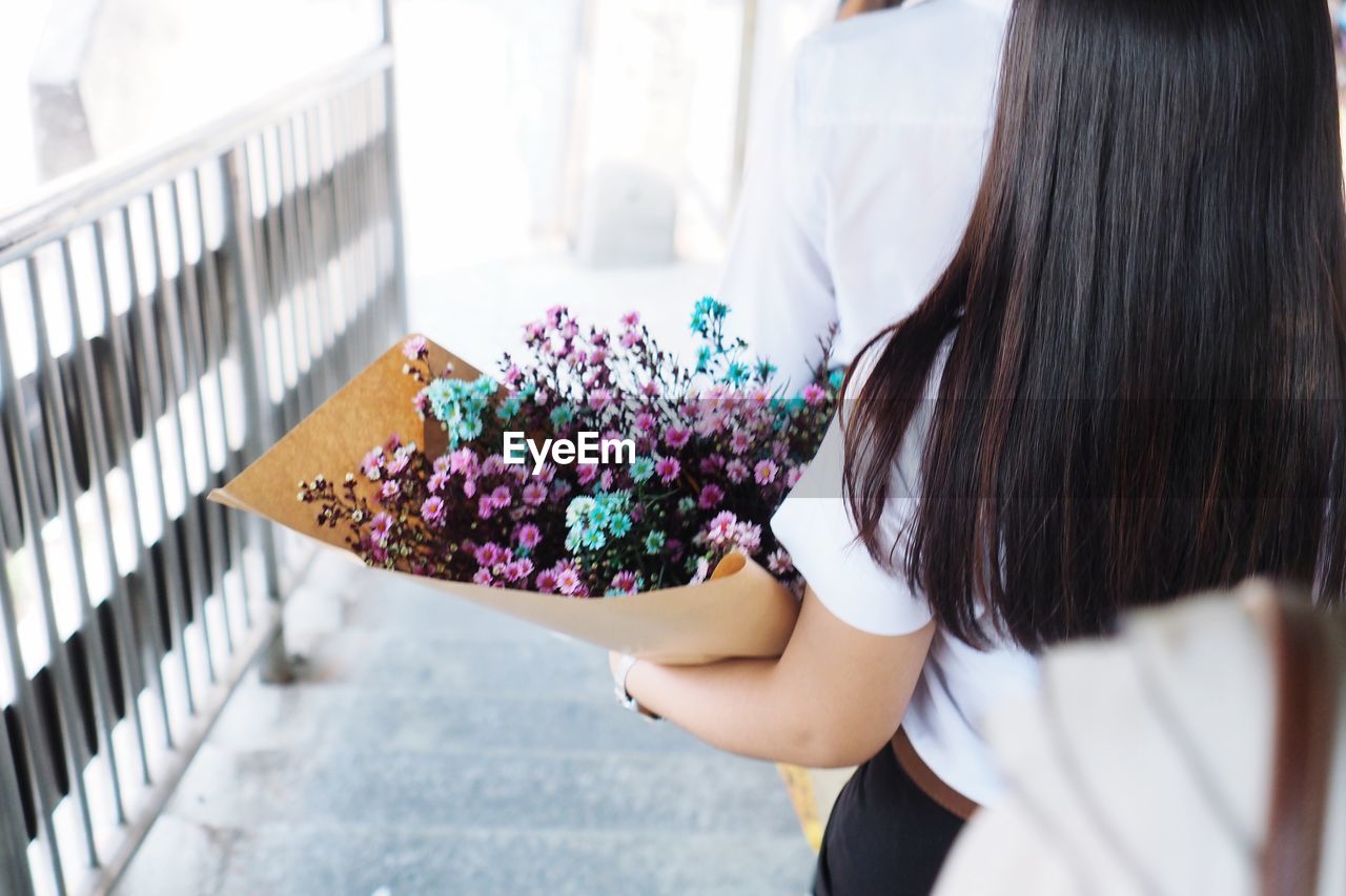 REAR VIEW OF WOMAN HOLDING FLOWERING PLANT