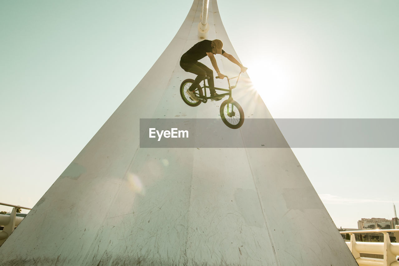 Man riding bicycle on built structure against sky