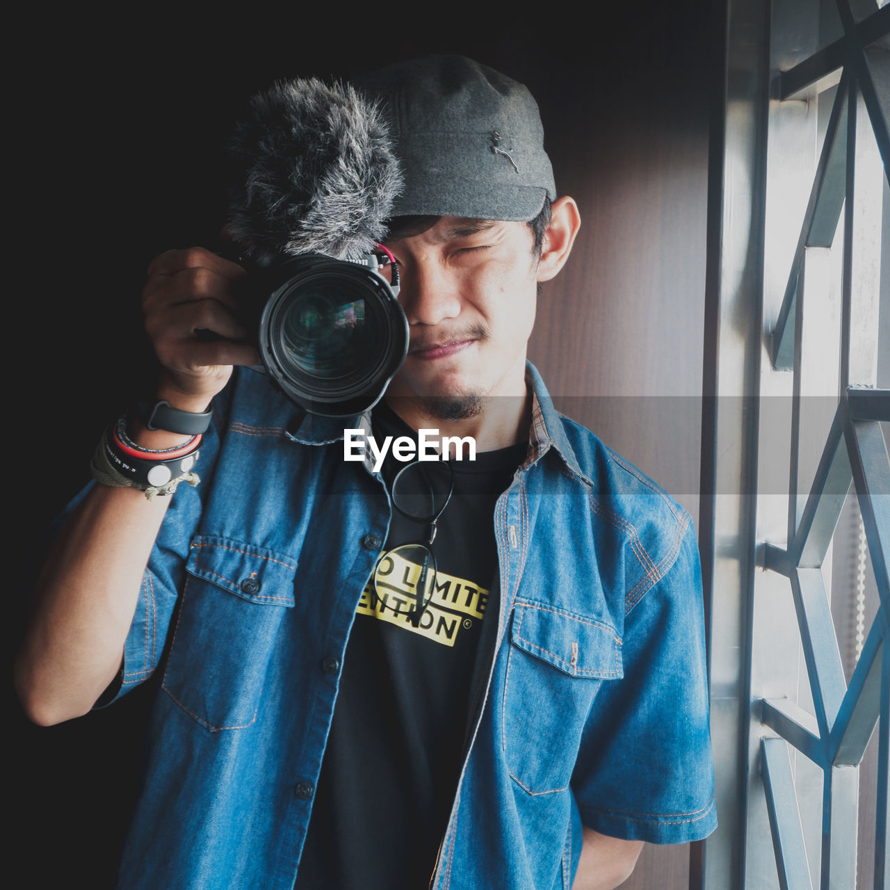 PORTRAIT OF YOUNG MAN HOLDING CAMERA WHILE STANDING AGAINST WALL