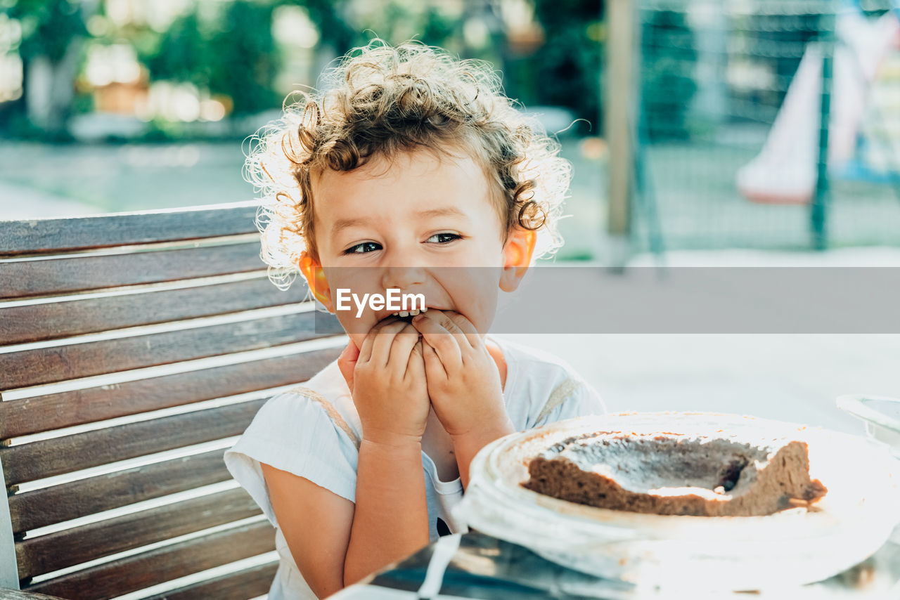 Cute girl eating sweet food while sitting outdoors