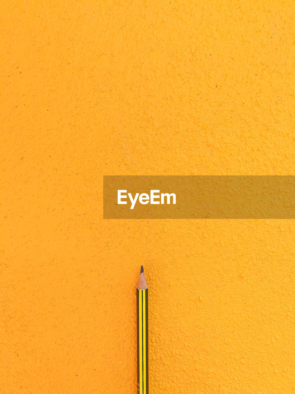 CLOSE-UP OF YELLOW PENCILS AGAINST WALL