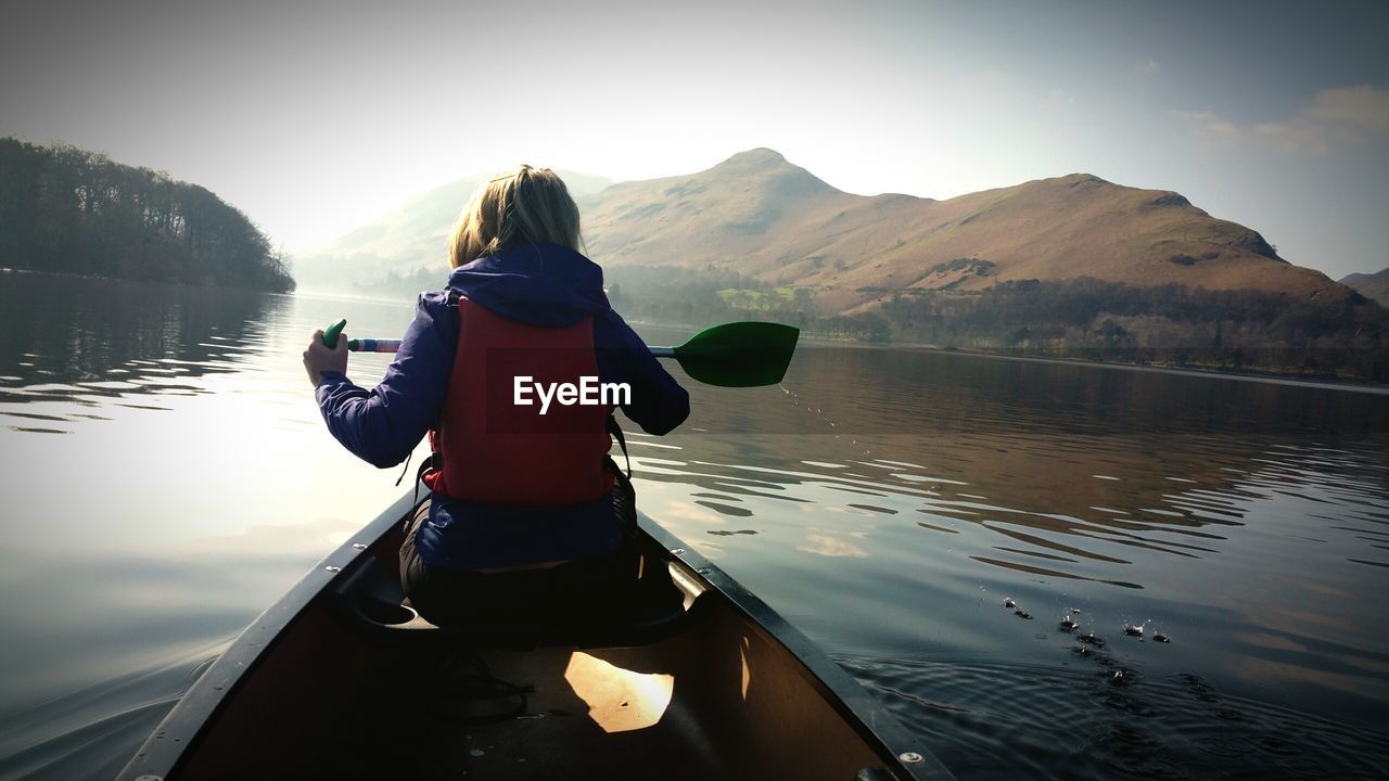 Rear view of woman boating in lake against mountains