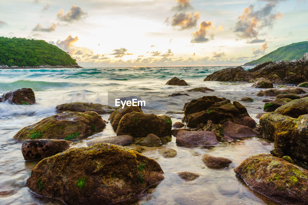 Rocks on beach against sky during sunset