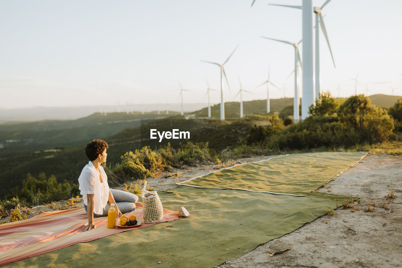 Woman looking at wind turbines while sitting on picnic blanket