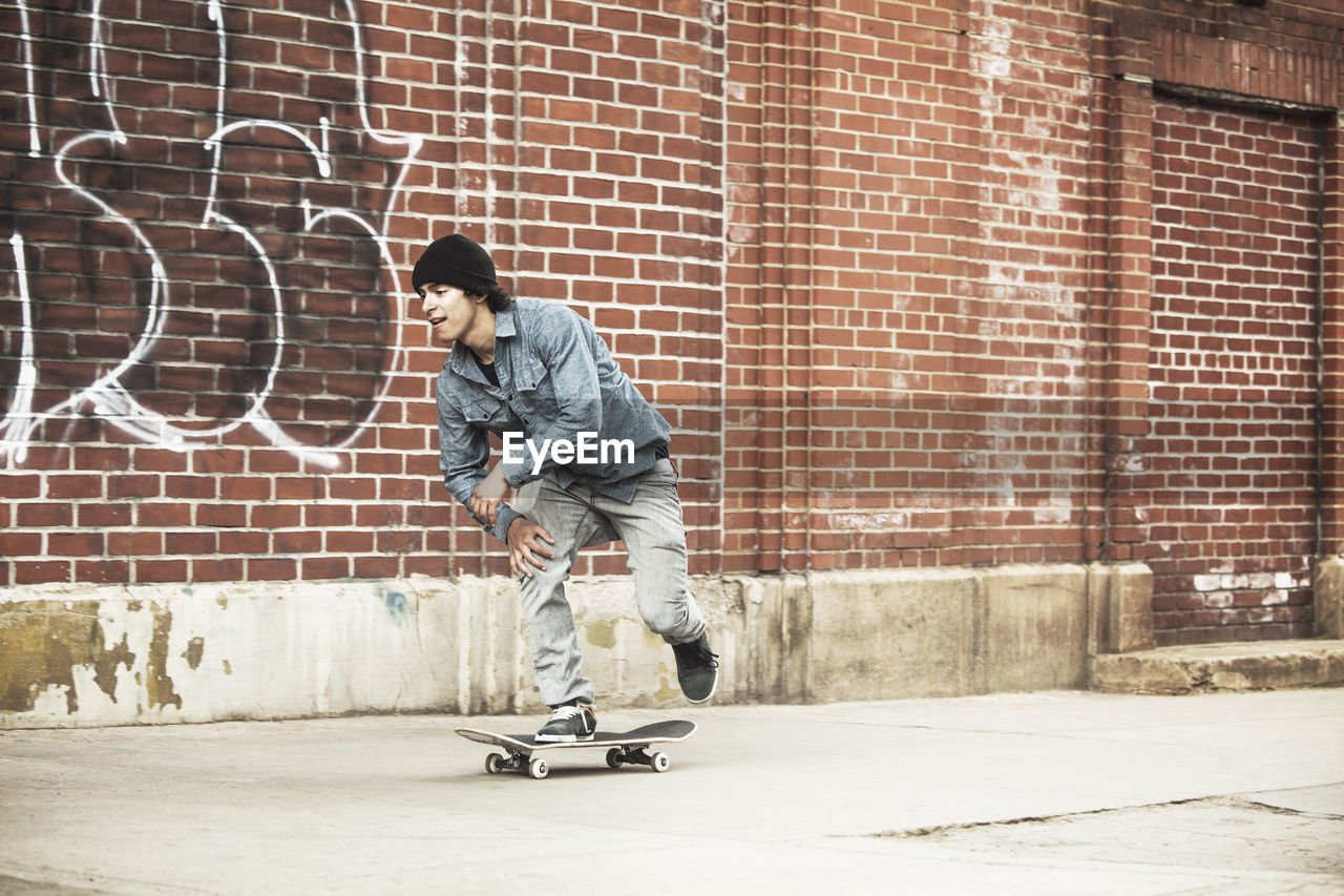 Man skateboarding on footpath against brick wall