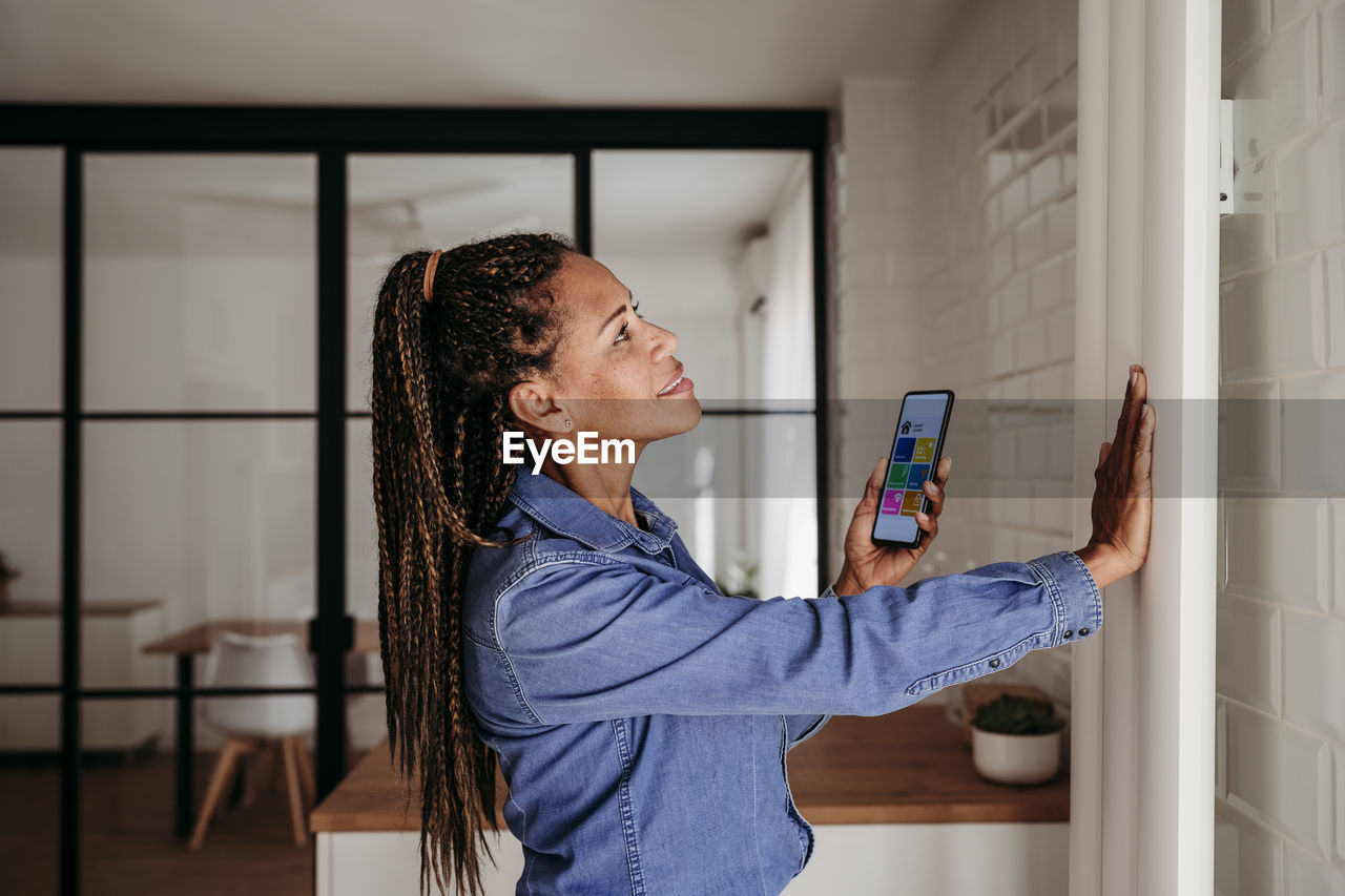 Smiling woman touching radiator standing with smart phone at home