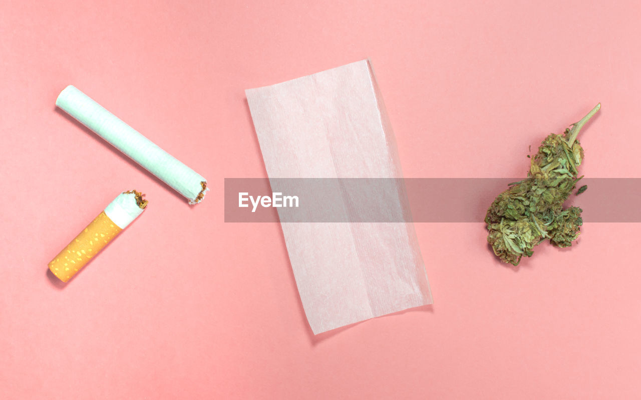 Materials to roll cannabis joint with tobacco on pink background.