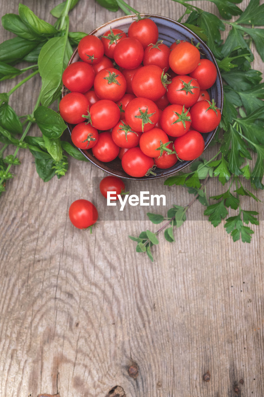 Fresh, organically homegrown cherry tomato harvest in a bowl with fresh herbs, basil and parsley