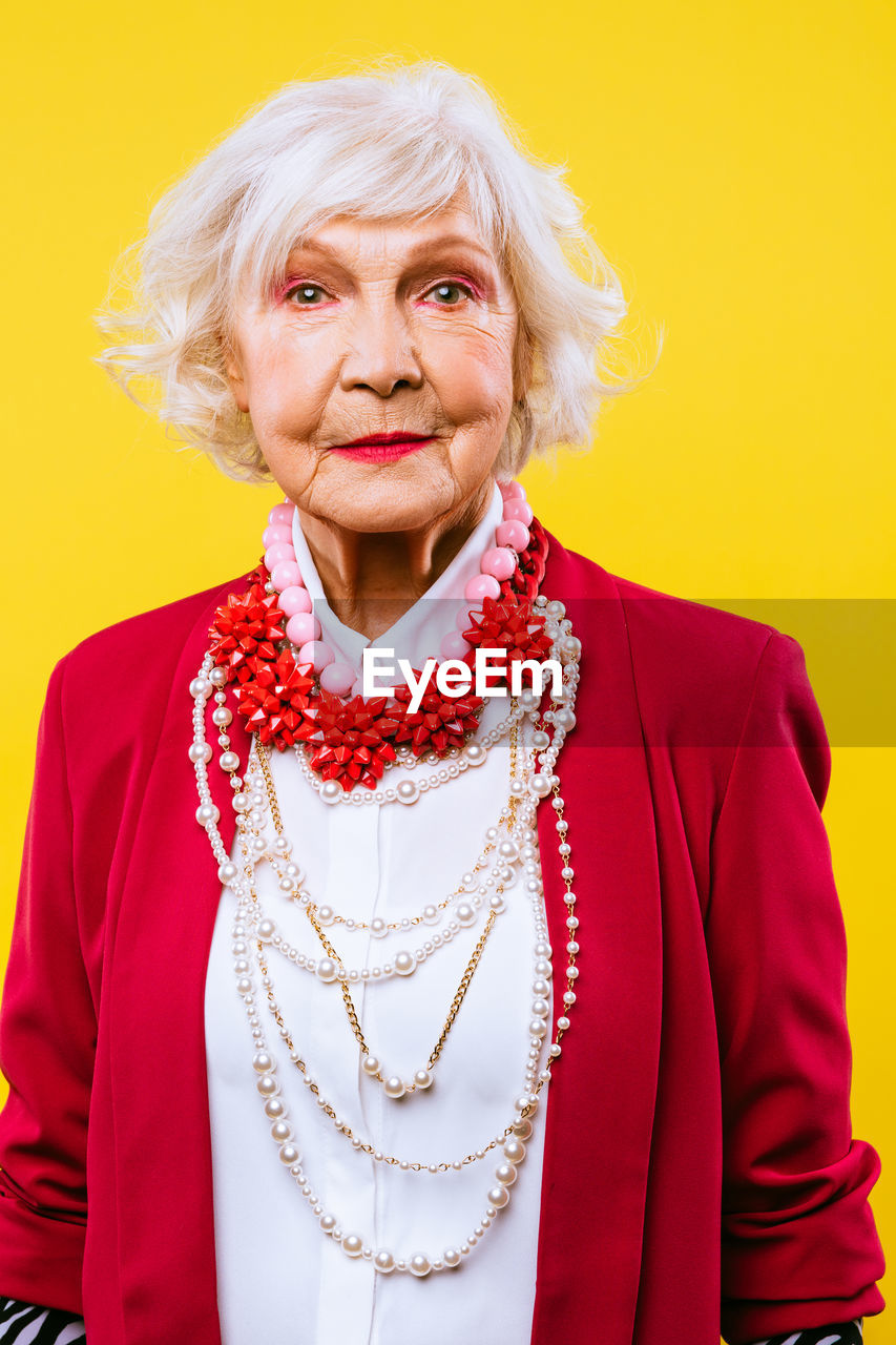 Portrait of senior woman standing against yellow background