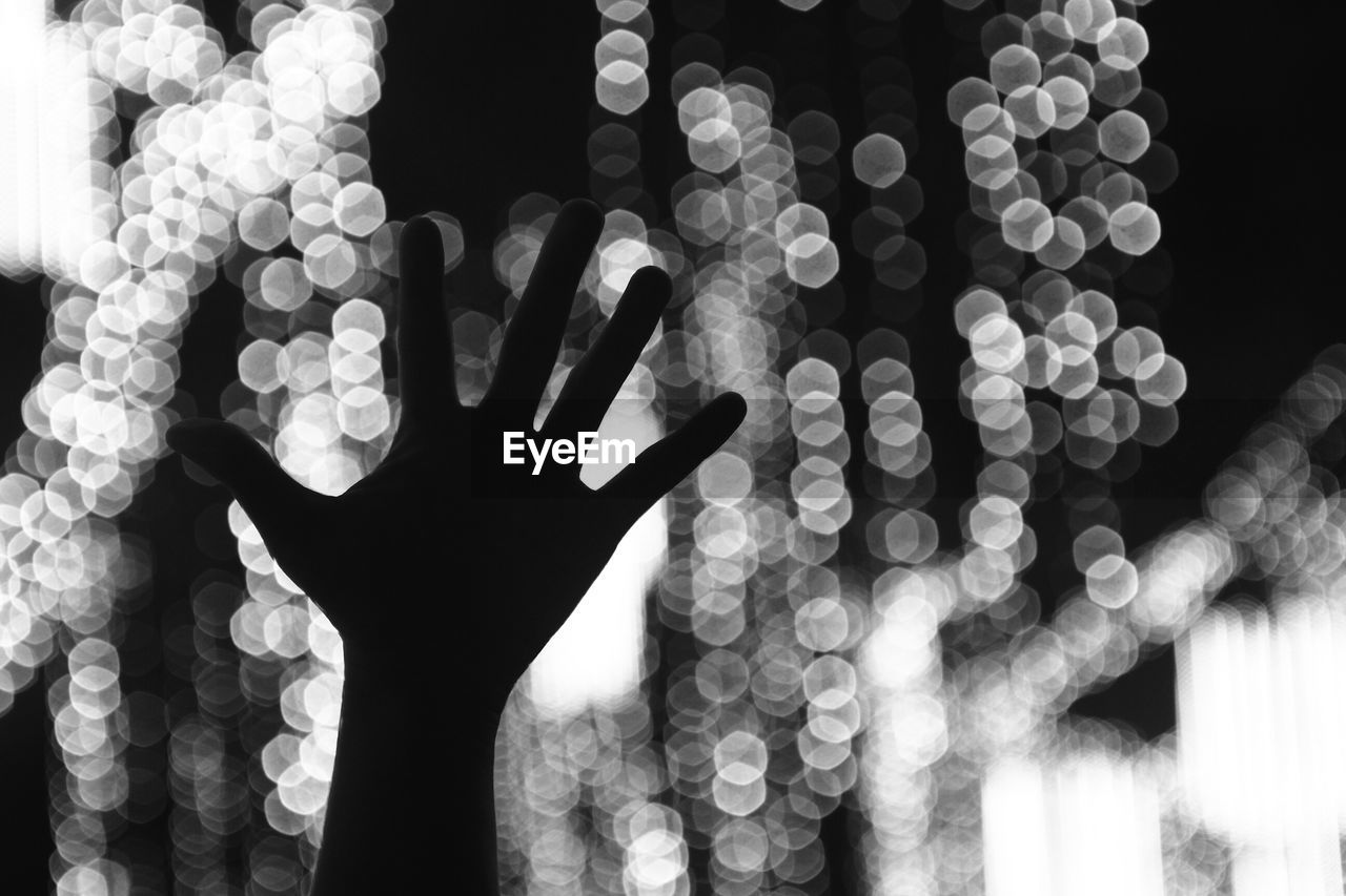 Cropped image of hand against illuminated lights at night