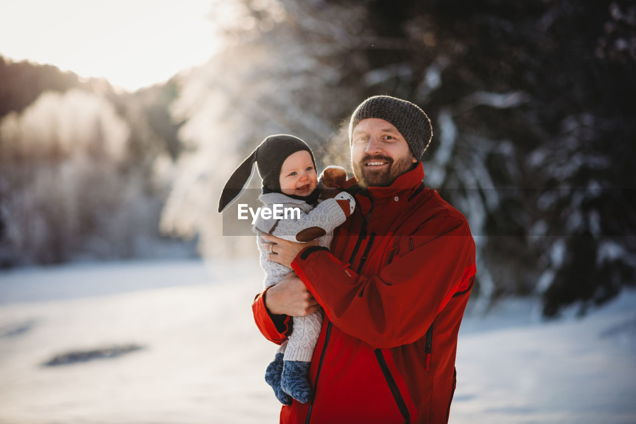 Father and baby smiling in winter wonderland full of snow in the woods