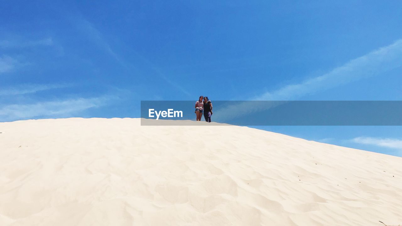 Low angle view of teenage girl standing with mother at desert on sunny day