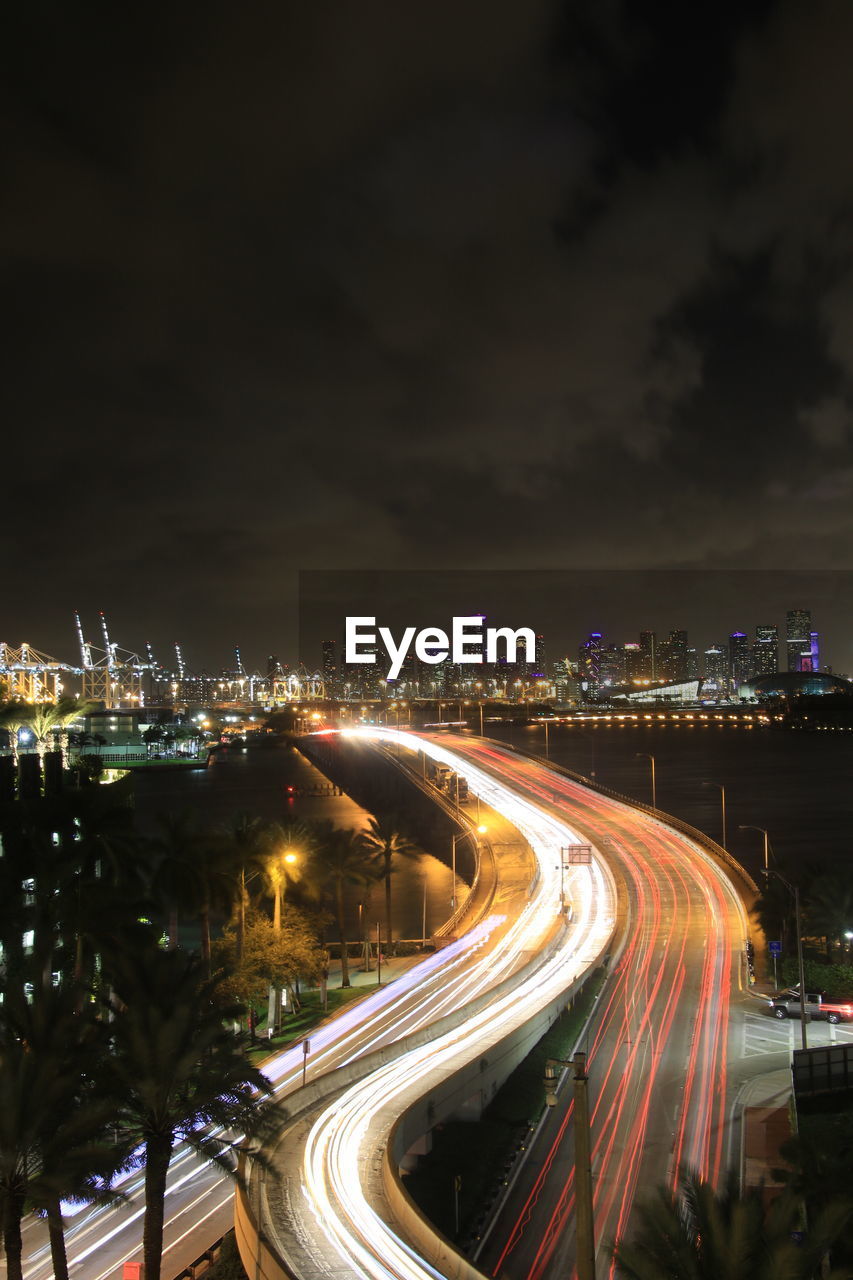 HIGH ANGLE VIEW OF LIGHT TRAILS ON ROAD AGAINST SKY