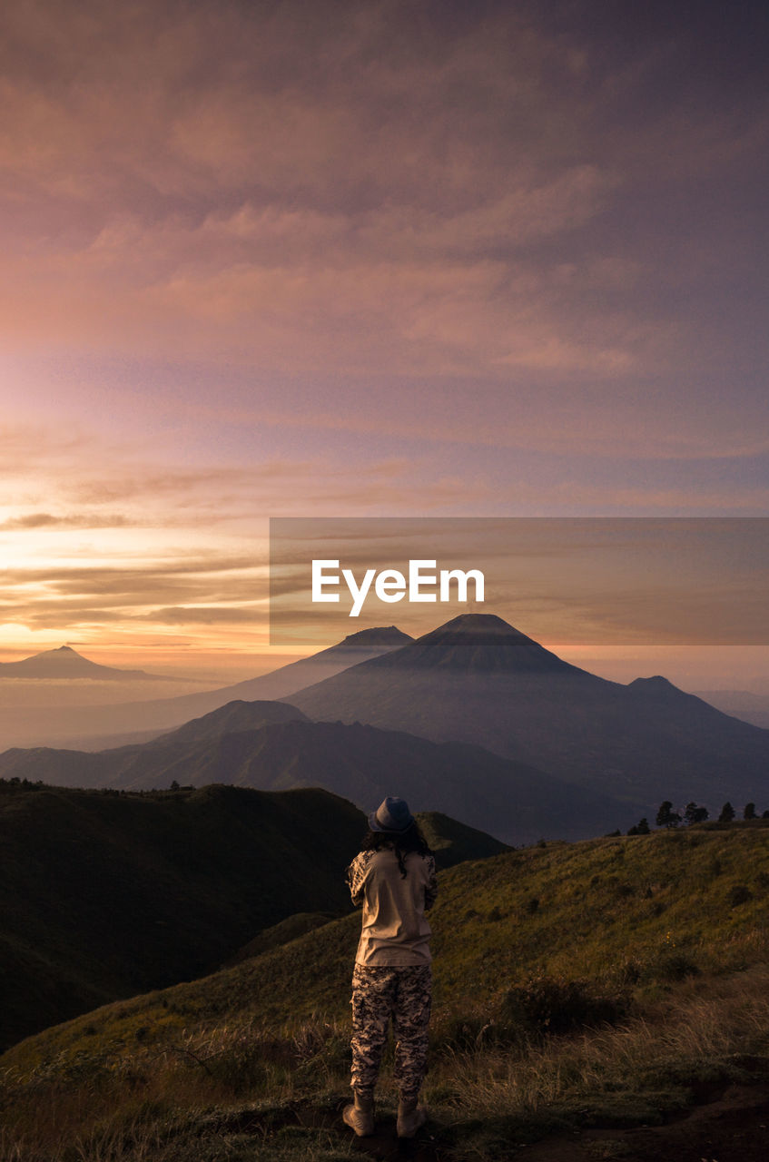 Rear view of man standing on mountain during sunset