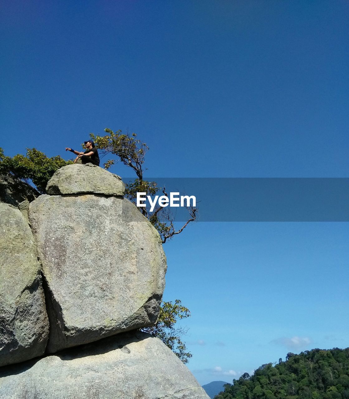 Low angle view of man sitting at the edge of cliff against clear sky