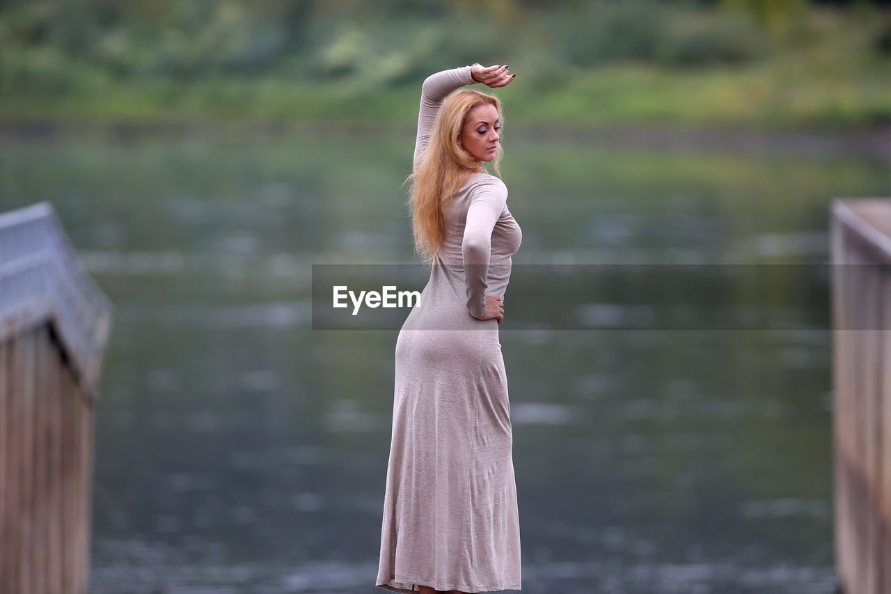 YOUNG WOMAN STANDING AGAINST WATER IN LAKE