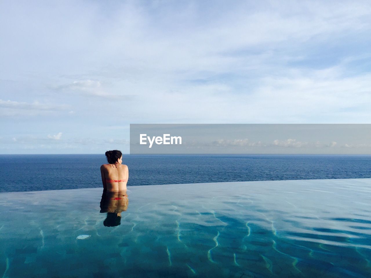 Rear view of woman in infinity pool against sea
