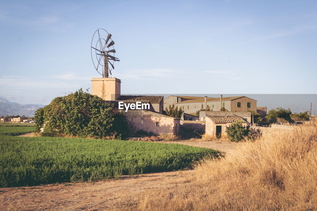 Traditional windmill by houses on field against sky