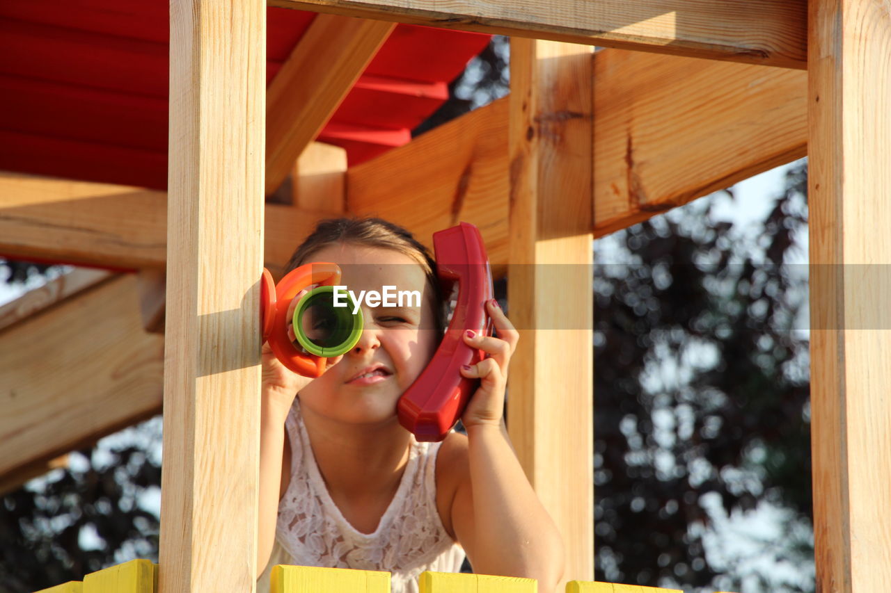 Girl talking on telephone while looking through telescope