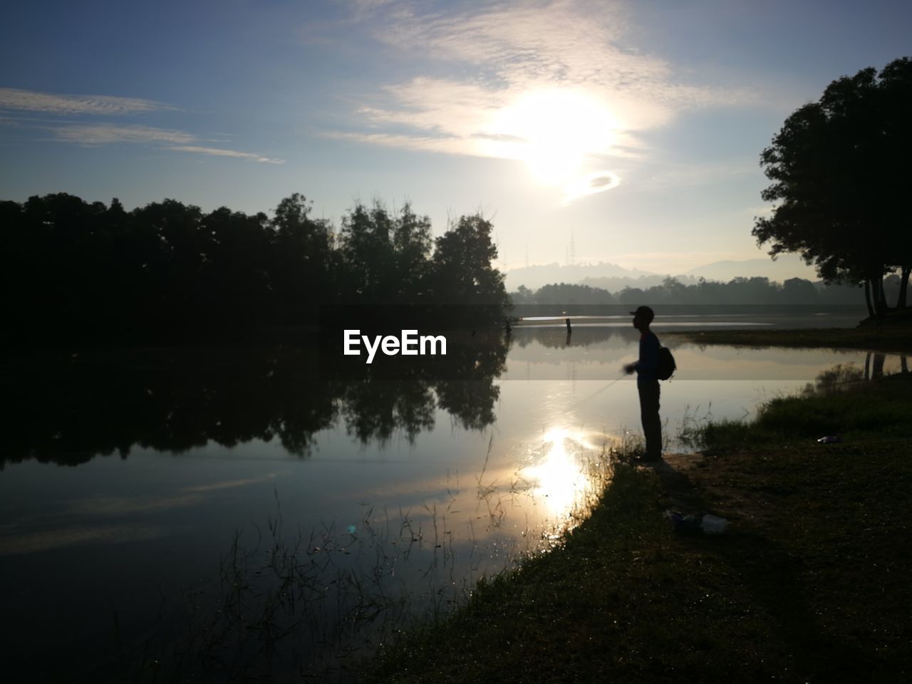 Silhouette of man standing by lake during sunset