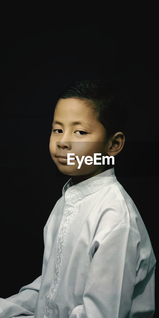 Portrait of boy looking away against black background