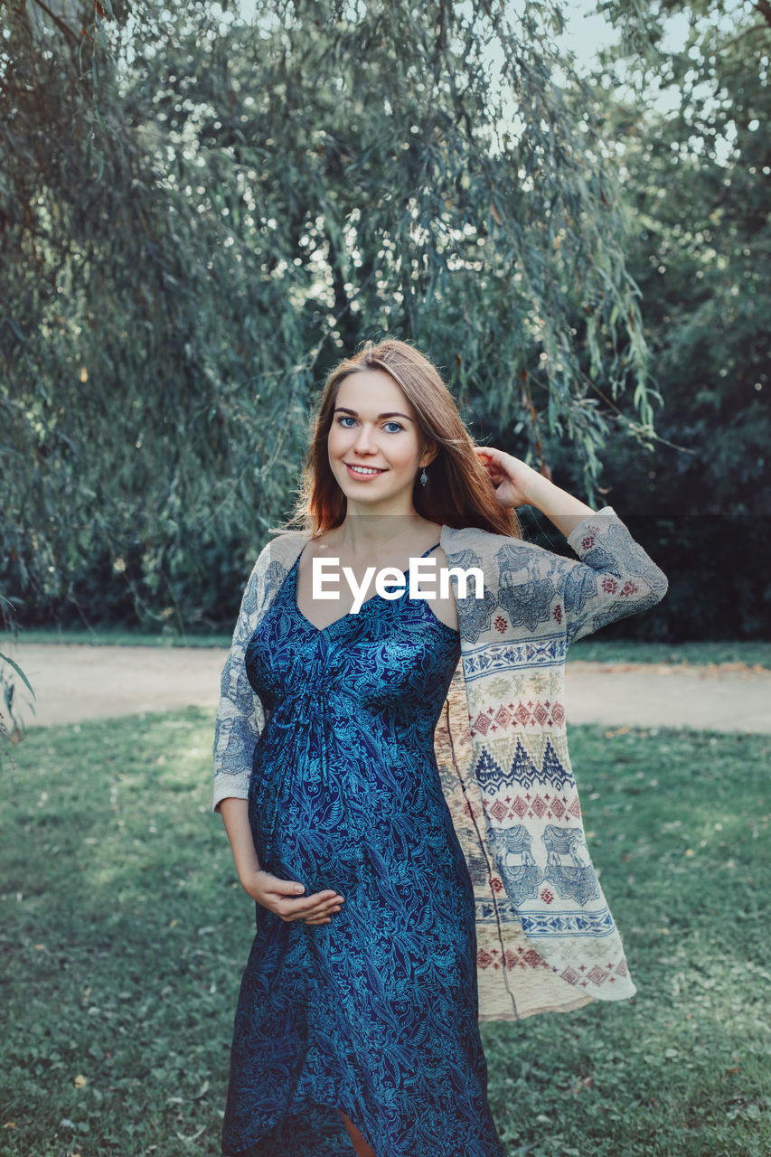 Portrait of smiling pregnant woman standing against trees