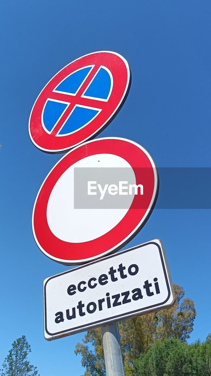 sign, blue, communication, road sign, traffic sign, sky, road, guidance, text, signage, no people, clear sky, nature, symbol, arrow symbol, low angle view, tree, street sign, red, western script, directional sign, day, information sign, outdoors, plant, traffic arrow sign, transportation, sunny, font