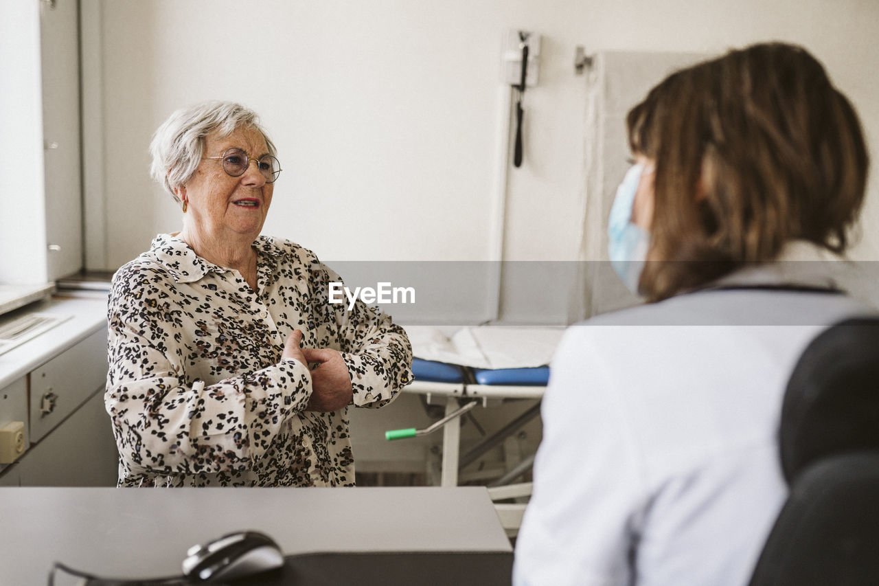 Senior female patient discussing with healthcare worker while consulting during covid-19