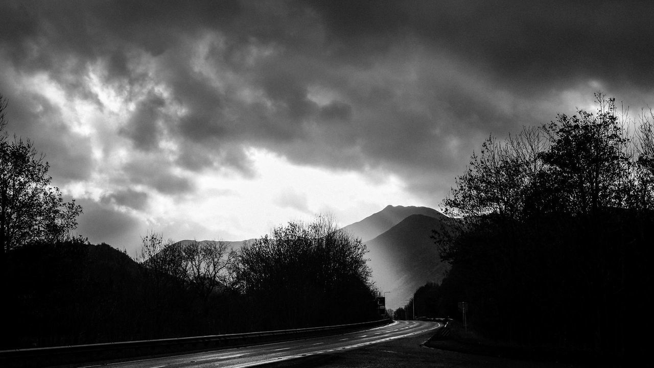 Road amidst silhouette trees against cloudy sky