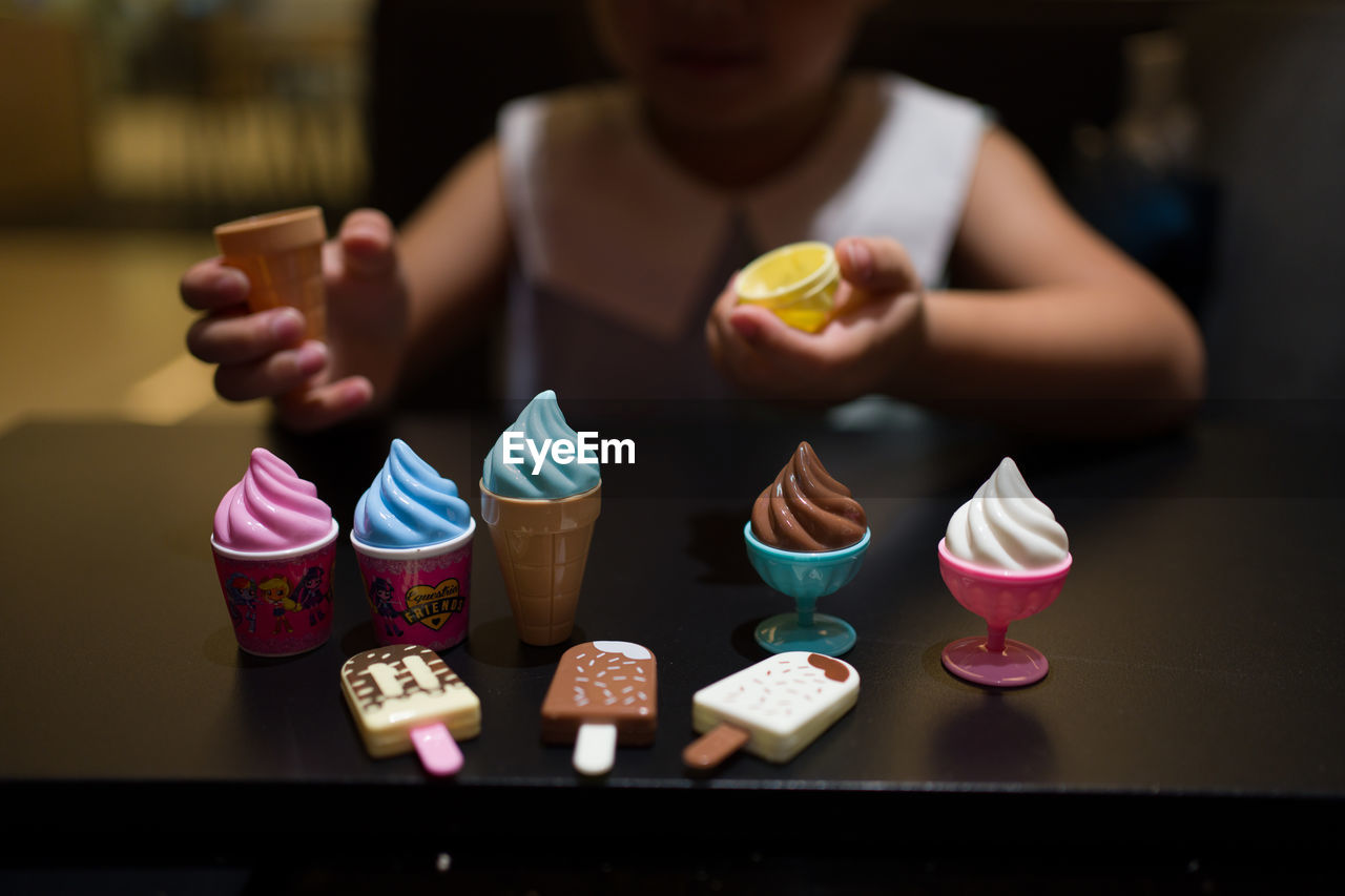 Midsection of girl with colorful ice cream toys at table